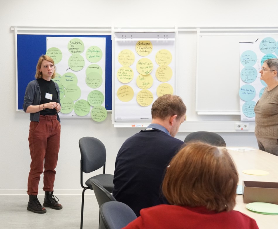 Diskussionsrunde mit Person vor Pinnwand mit zahlreichen Zetteln, Szene aus Workshop 2